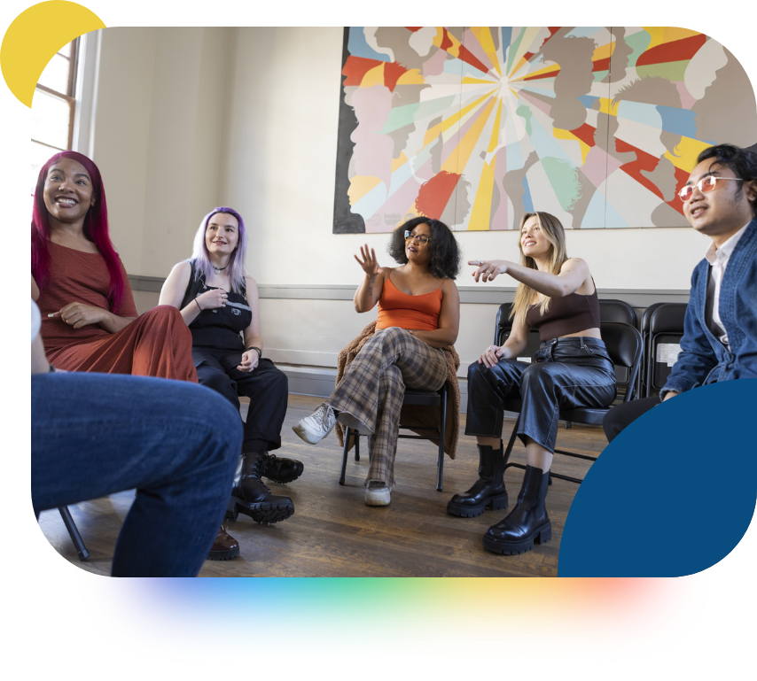 A group of young people sitting in a circle discussing something, smiling. 