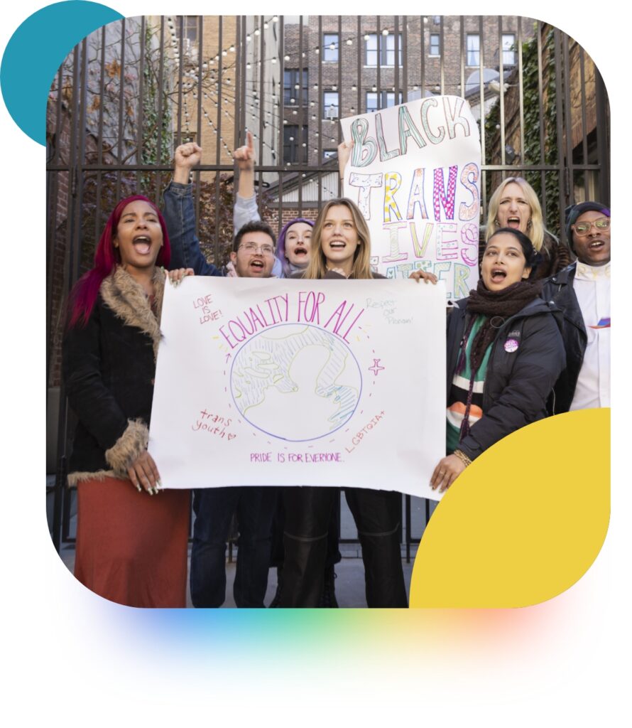 A diverse group of young people standing in the street in a circle, holding signs that read "Black trans lives matter", "Equality for all", "Love is love", "Pride is for everyone". 